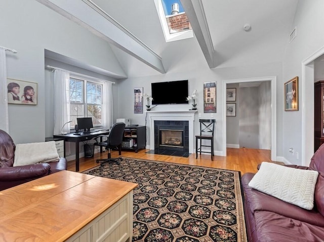 living area with a skylight, visible vents, baseboards, a tiled fireplace, and light wood-style flooring