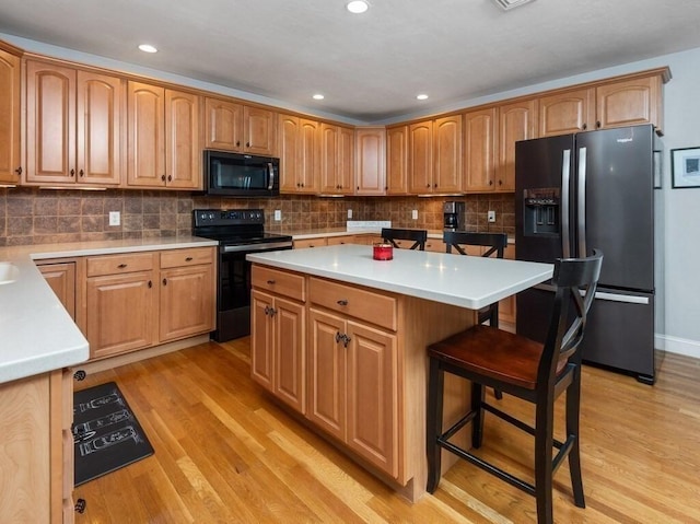 kitchen featuring black appliances, light countertops, light wood-style floors, and a kitchen breakfast bar