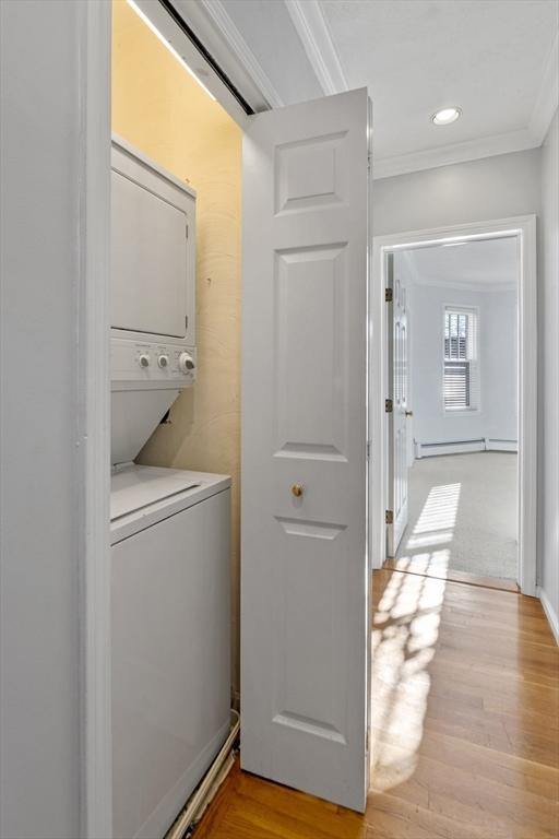 laundry room with light hardwood / wood-style floors, crown molding, stacked washer / dryer, and a baseboard heating unit