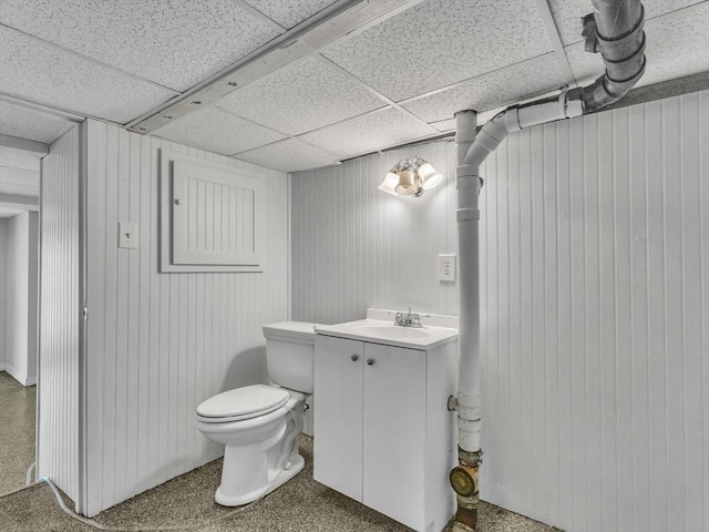half bathroom with vanity, wood walls, a drop ceiling, and toilet