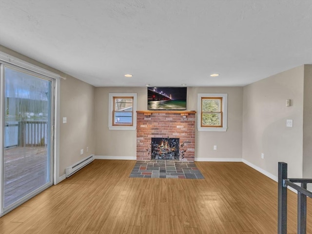 unfurnished living room featuring baseboards, a baseboard heating unit, a wealth of natural light, and light wood-style floors