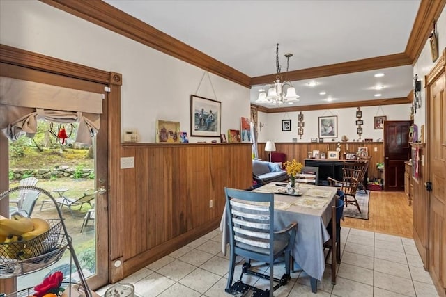dining room with ornamental molding, a wainscoted wall, a chandelier, light tile patterned flooring, and wood walls