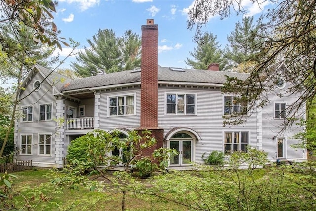 back of property with a balcony, a chimney, and french doors