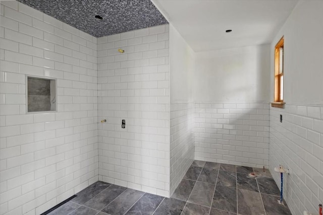 bathroom featuring tile walls, a wainscoted wall, and tiled shower
