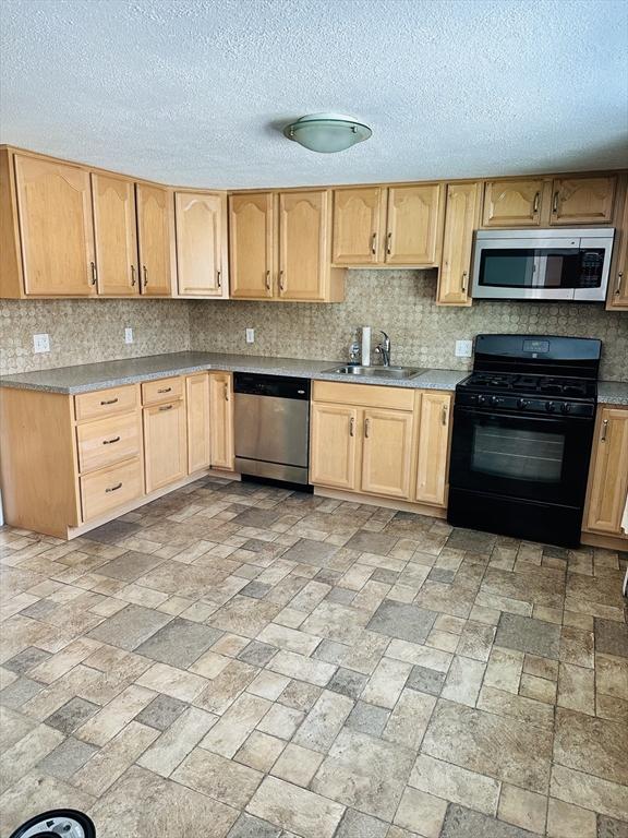 kitchen with stainless steel appliances, light countertops, decorative backsplash, light brown cabinets, and a sink