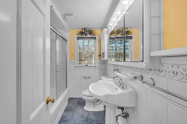 full bathroom featuring sink, tile patterned flooring, enclosed tub / shower combo, toilet, and tile walls