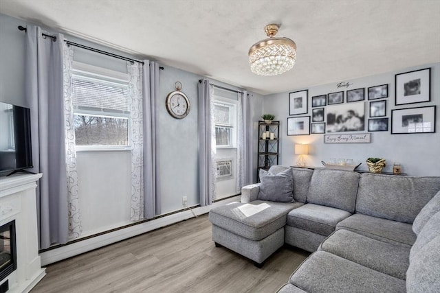 living area with a chandelier, a glass covered fireplace, baseboard heating, and wood finished floors