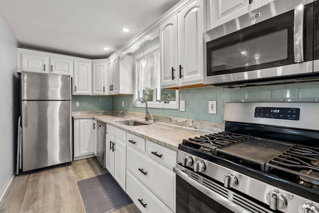 kitchen featuring white cabinets, appliances with stainless steel finishes, light stone countertops, light wood-style floors, and a sink