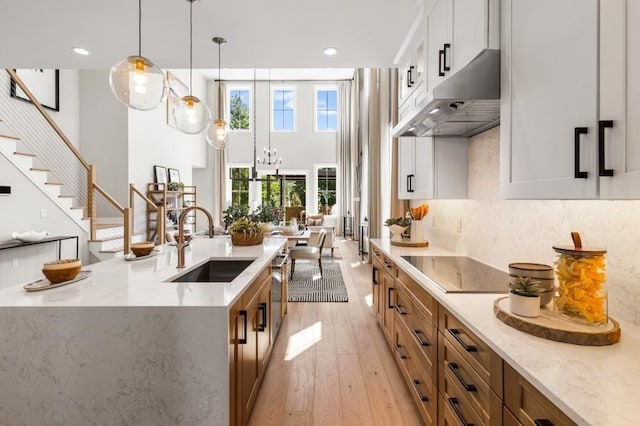 kitchen with pendant lighting, a sink, light stone counters, under cabinet range hood, and light wood finished floors