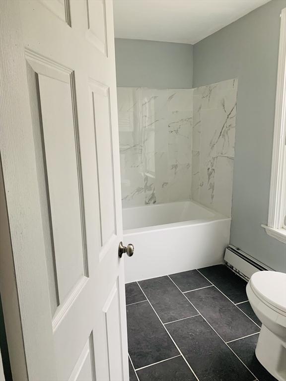 bathroom featuring tiled shower / bath combo, toilet, tile patterned floors, and a baseboard heating unit