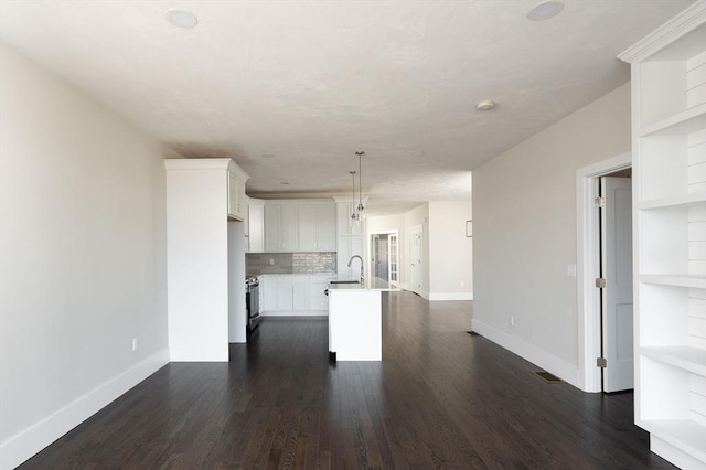 kitchen featuring dark wood-type flooring, tasteful backsplash, pendant lighting, a kitchen island with sink, and white cabinets