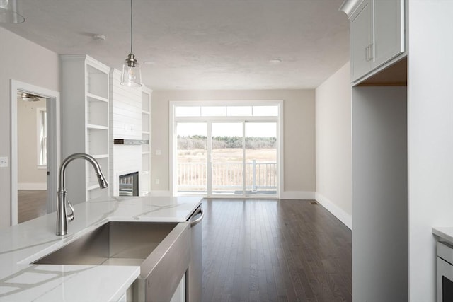 kitchen with light stone countertops, dark wood-type flooring, sink, decorative light fixtures, and white cabinetry