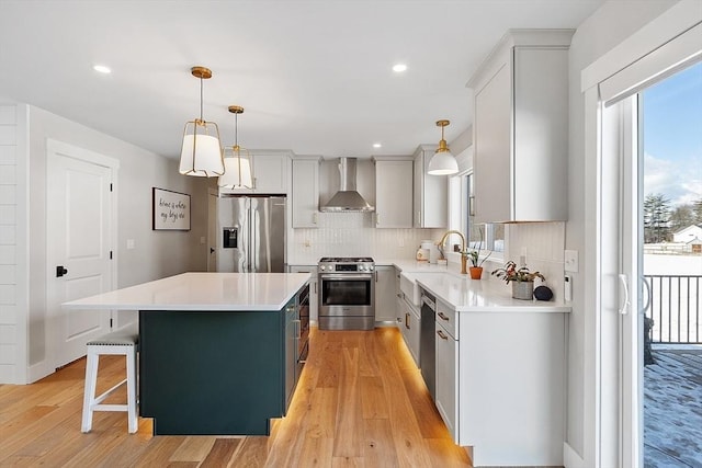 kitchen featuring a kitchen island, appliances with stainless steel finishes, a breakfast bar, pendant lighting, and wall chimney exhaust hood