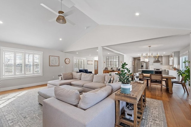 living room with high vaulted ceiling, ceiling fan with notable chandelier, and light wood-type flooring