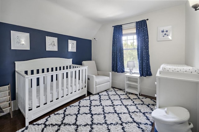 bedroom with lofted ceiling, wood finished floors, baseboards, and a nursery area