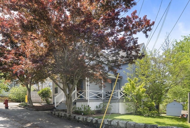 view of side of home featuring a porch, a shed, an outbuilding, and a lawn
