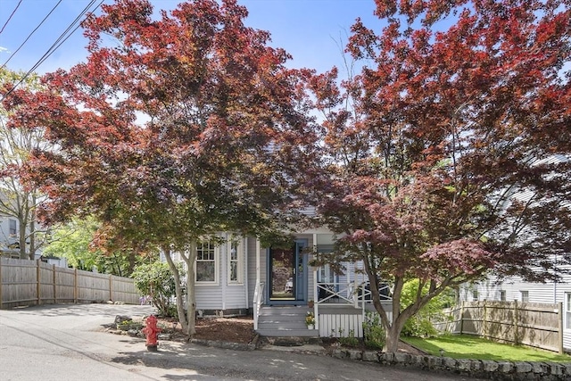 view of property hidden behind natural elements featuring a porch and fence