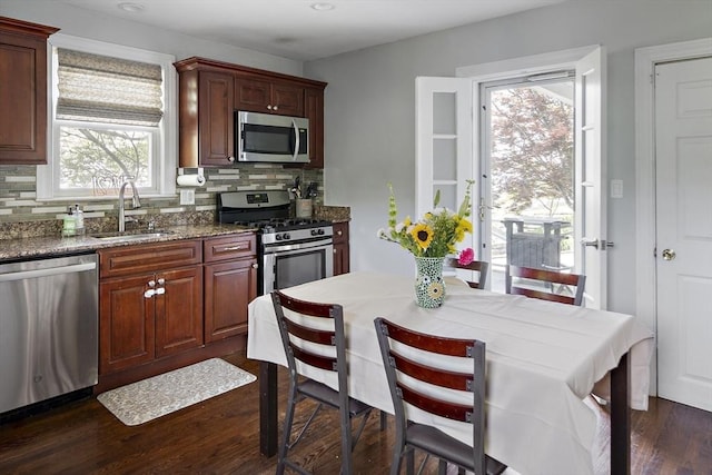 kitchen with stainless steel appliances, a sink, decorative backsplash, dark wood-style flooring, and dark stone counters