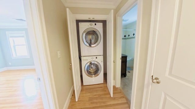 laundry room featuring baseboards, ornamental molding, laundry area, stacked washer and dryer, and light wood finished floors
