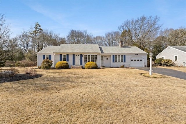 single story home featuring aphalt driveway, a front yard, a chimney, and a garage