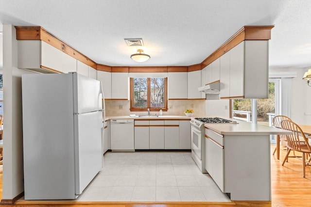 kitchen featuring under cabinet range hood, white appliances, a sink, visible vents, and light countertops