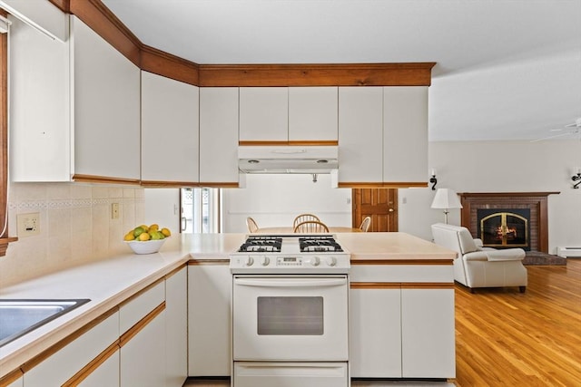 kitchen featuring white range with gas cooktop, white cabinets, light countertops, under cabinet range hood, and a fireplace