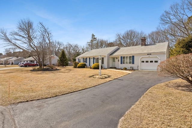 view of front of home with a garage, driveway, a chimney, and a front yard