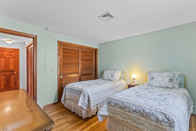 bedroom with a closet, wood finished floors, visible vents, and attic access