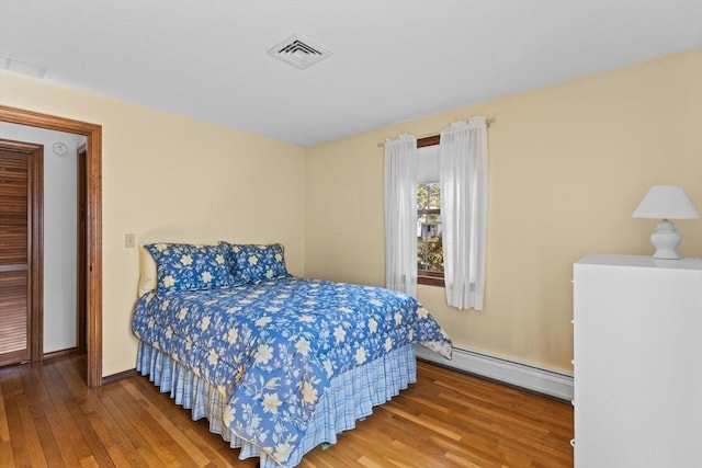 bedroom with a baseboard radiator, wood-type flooring, visible vents, and baseboards