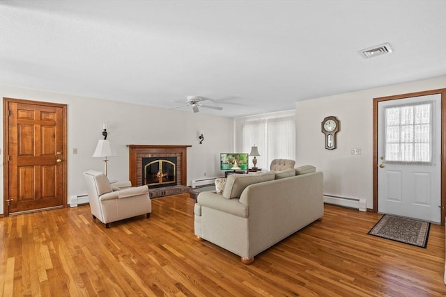 living room with light wood finished floors, a baseboard radiator, and a brick fireplace