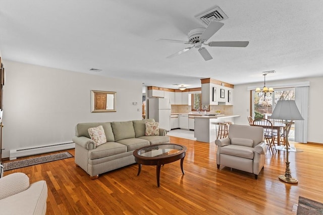 living room with light wood-style floors, visible vents, and baseboard heating