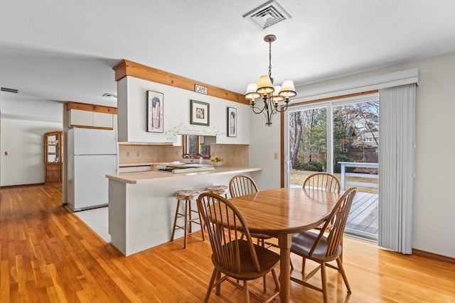 dining area featuring a chandelier, a textured ceiling, visible vents, baseboards, and light wood finished floors