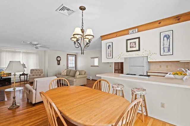 dining area with ceiling fan with notable chandelier, a baseboard radiator, wood finished floors, and visible vents