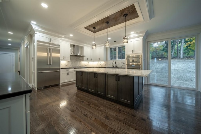 kitchen with pendant lighting, wall chimney exhaust hood, white cabinets, and stainless steel appliances