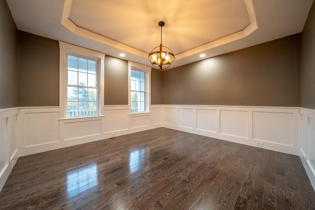 spare room with a raised ceiling, dark hardwood / wood-style flooring, and a chandelier