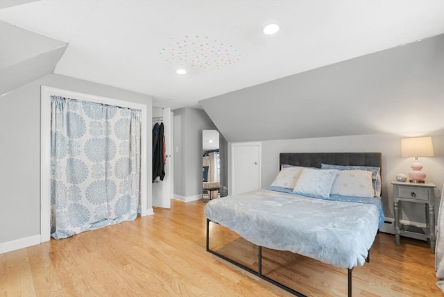 bedroom with a walk in closet, a closet, lofted ceiling, and light wood-type flooring