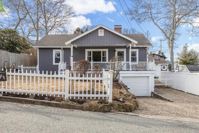 view of front of home with a porch, roof with shingles, a fenced front yard, and a chimney