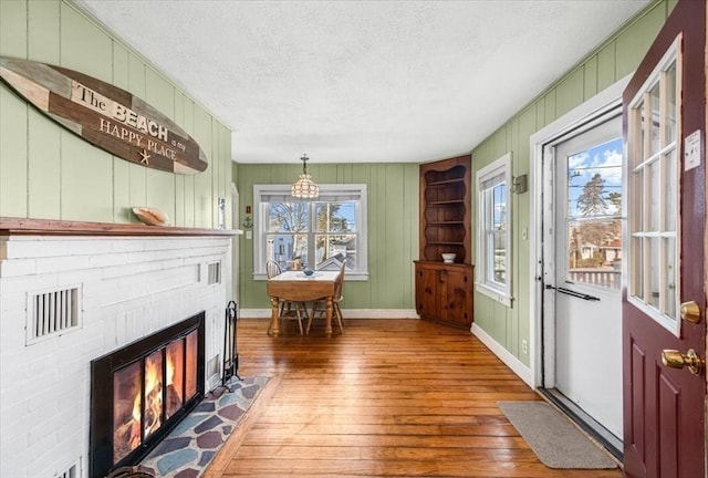 interior space with visible vents, hardwood / wood-style flooring, a textured ceiling, baseboards, and a brick fireplace