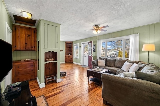 living area with baseboards, a textured ceiling, light wood-style floors, and a ceiling fan