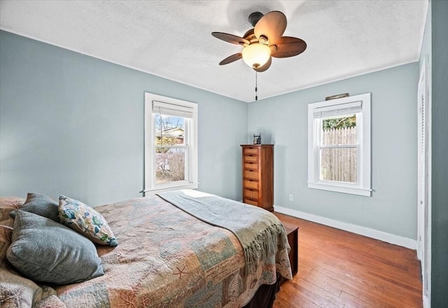 bedroom featuring baseboards, multiple windows, a textured ceiling, and wood-type flooring