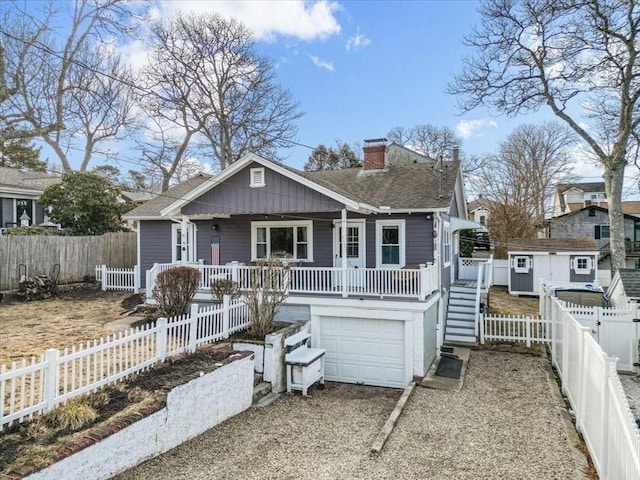 view of front facade with driveway, a porch, a shingled roof, a chimney, and fence private yard