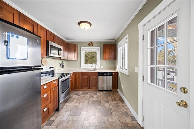 kitchen featuring stone finish flooring, appliances with stainless steel finishes, crown molding, light countertops, and baseboards