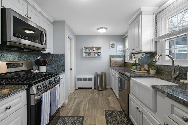 kitchen featuring light wood-type flooring, stainless steel appliances, sink, white cabinets, and radiator heating unit