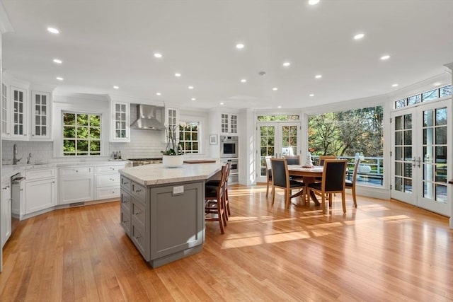 kitchen with white cabinetry, french doors, appliances with stainless steel finishes, a center island, and wall chimney exhaust hood