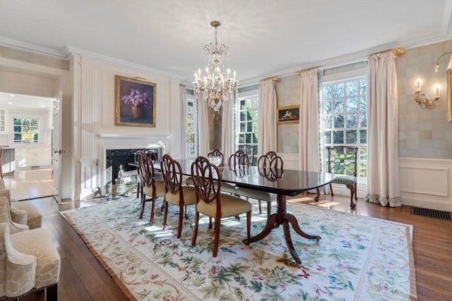 dining space featuring a wainscoted wall, a fireplace, crown molding, and wood finished floors