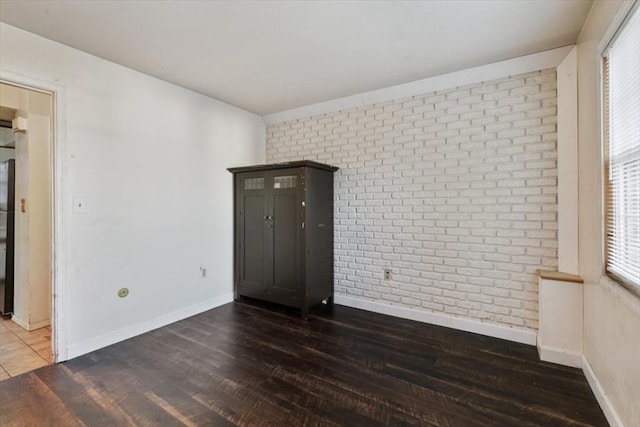 unfurnished room with dark wood-type flooring and brick wall