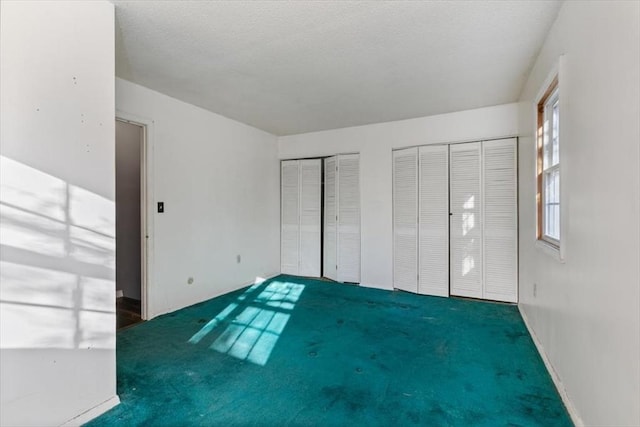 unfurnished bedroom with dark colored carpet and two closets