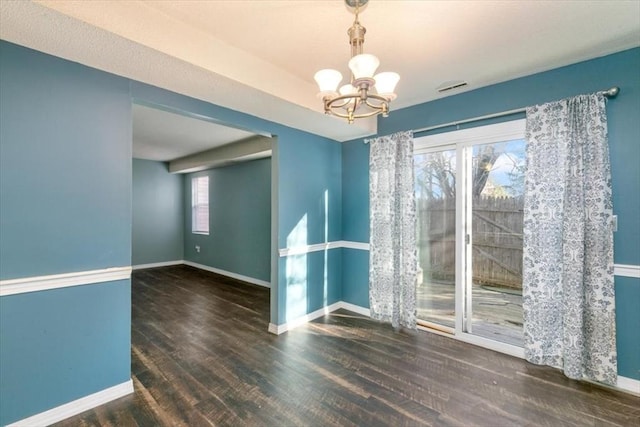 spare room featuring a healthy amount of sunlight, dark hardwood / wood-style flooring, and a notable chandelier