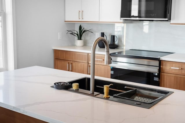 kitchen with brown cabinets, appliances with stainless steel finishes, white cabinetry, and light stone countertops