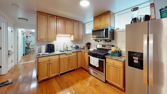 kitchen with light stone countertops, appliances with stainless steel finishes, sink, and light hardwood / wood-style flooring